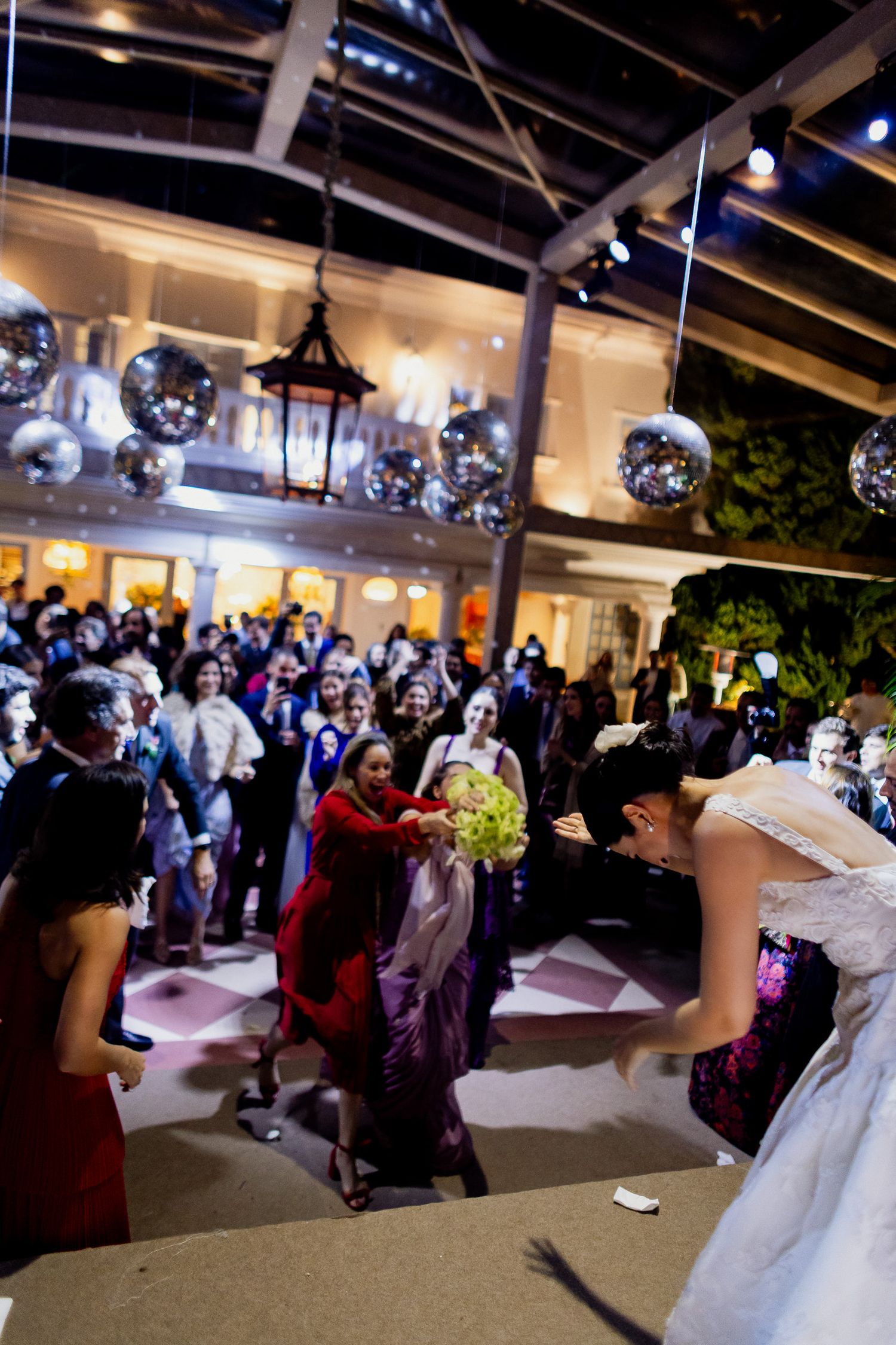 Wedding guests dance and celebrate on an outdoor patio decorated with disco balls and ambient lighting at night.