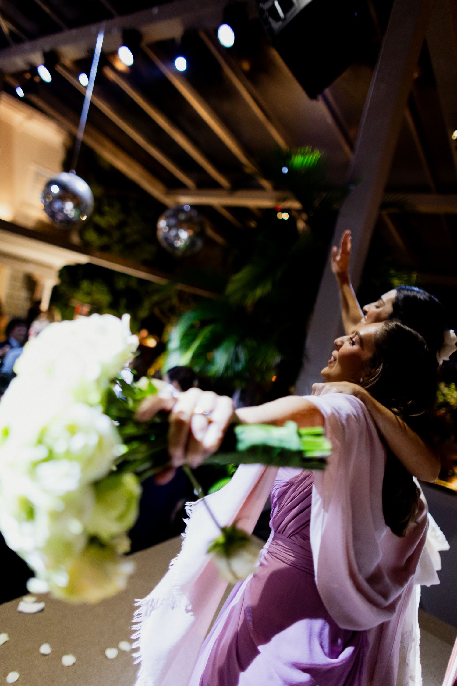 A person in a purple dress catches a white bridal bouquet during a wedding reception.