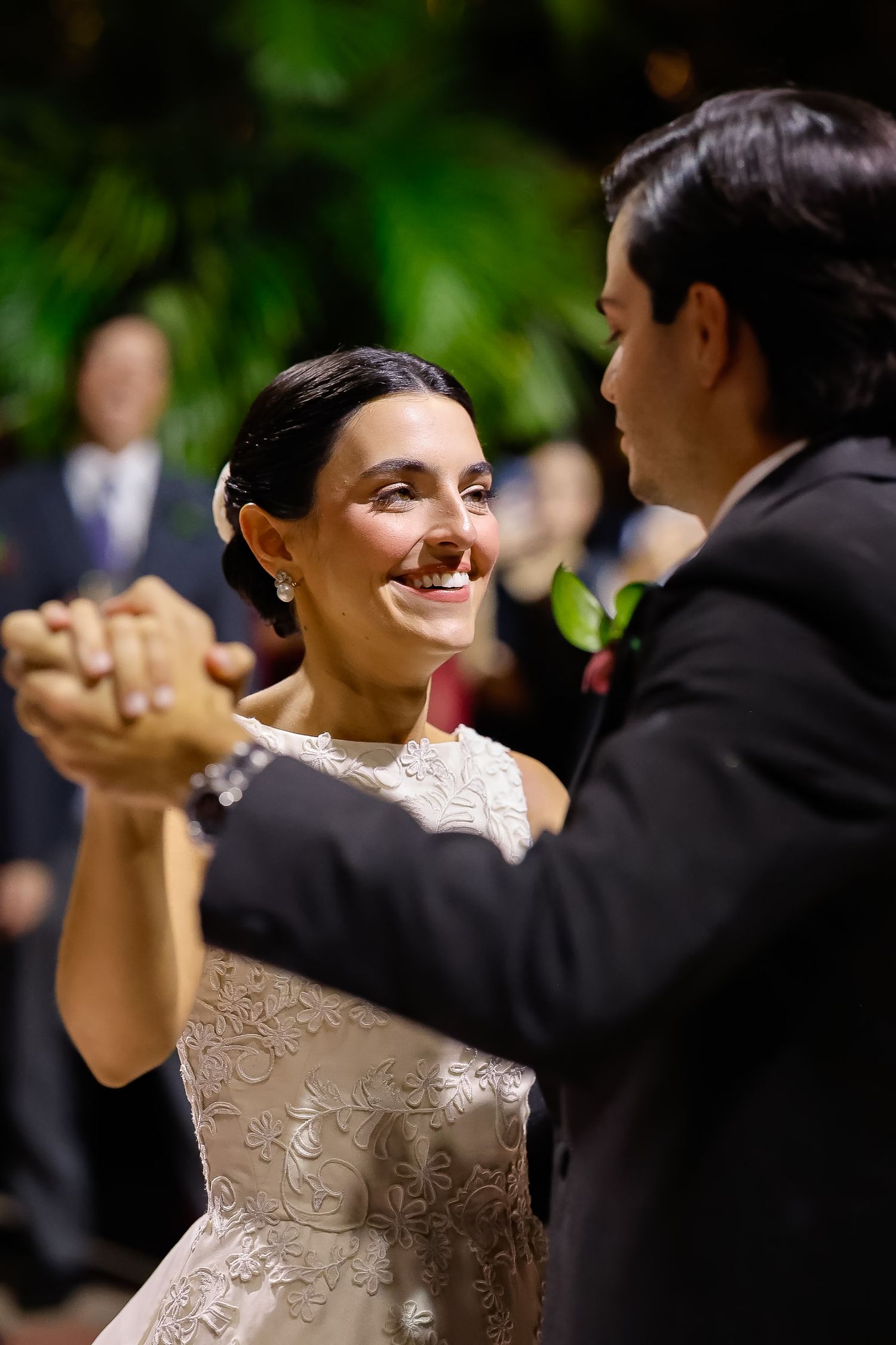 A couple dances together at a wedding celebration, with the bride wearing a delicate lace dress in an outdoor setting.
