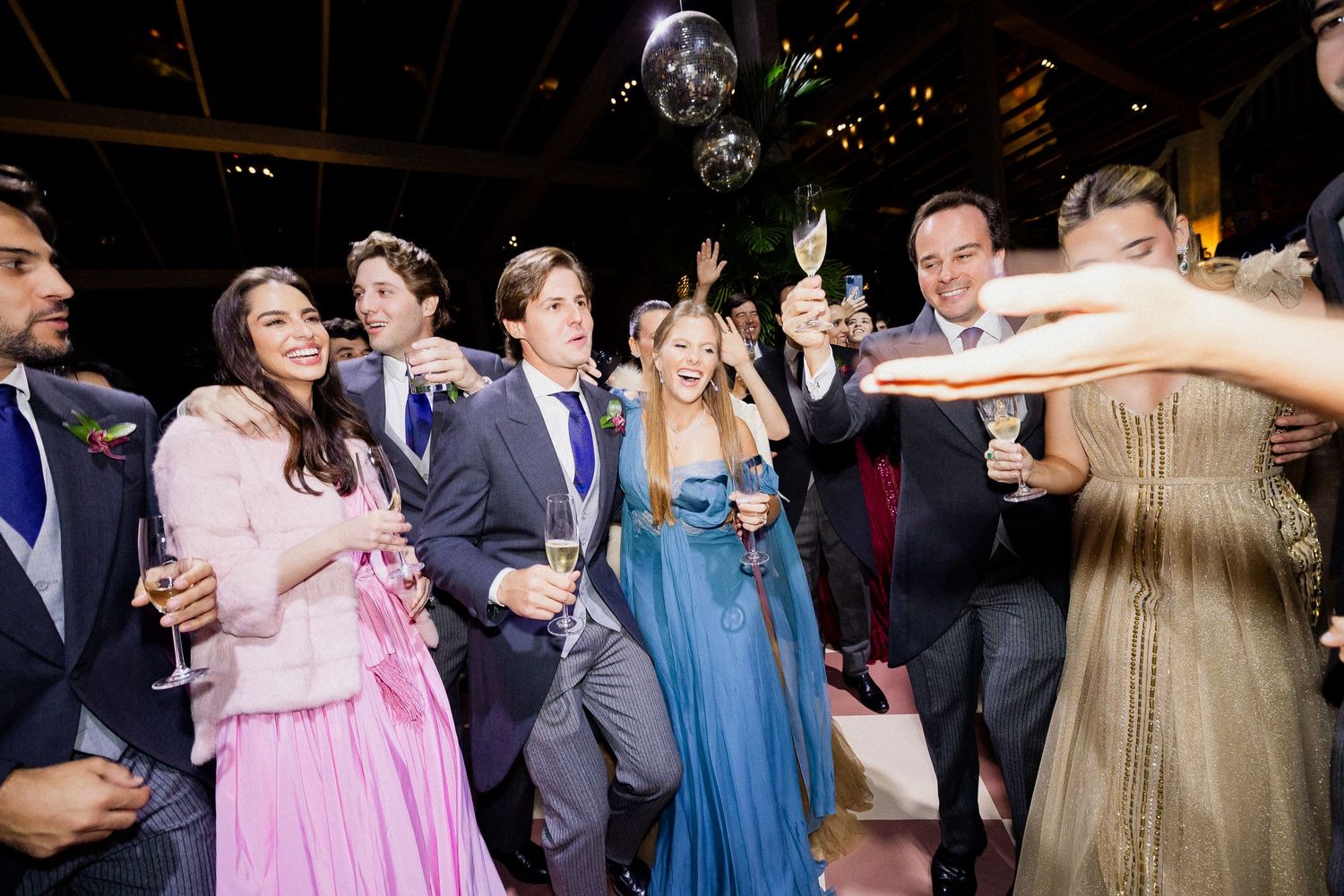 Wedding guests dancing and celebrating on a dance floor at a reception party with disco lights overhead.