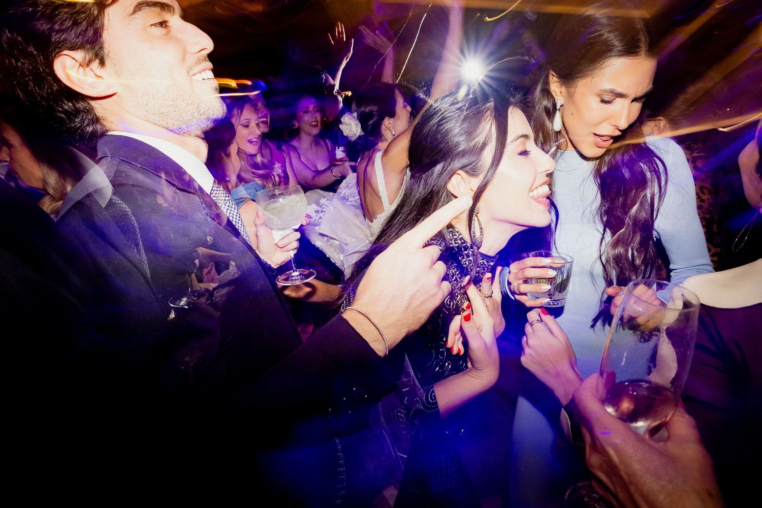 People dancing and celebrating at a nightclub with colorful purple lighting and energetic atmosphere.