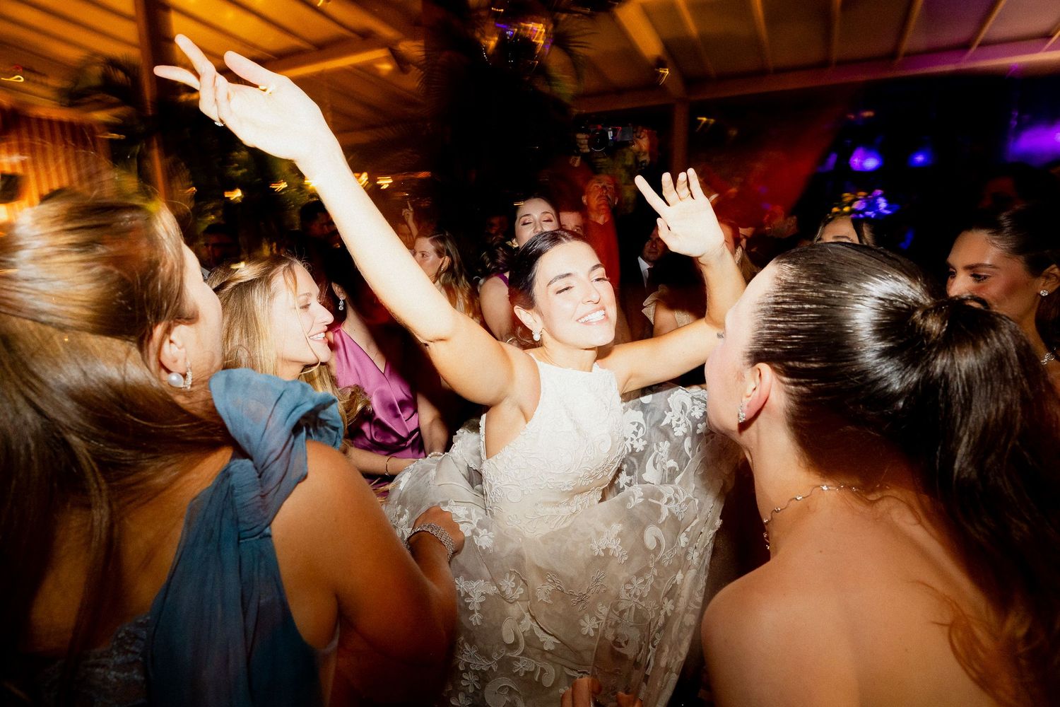 Wedding reception guests dancing and celebrating on a dark dance floor with colorful lighting effects.