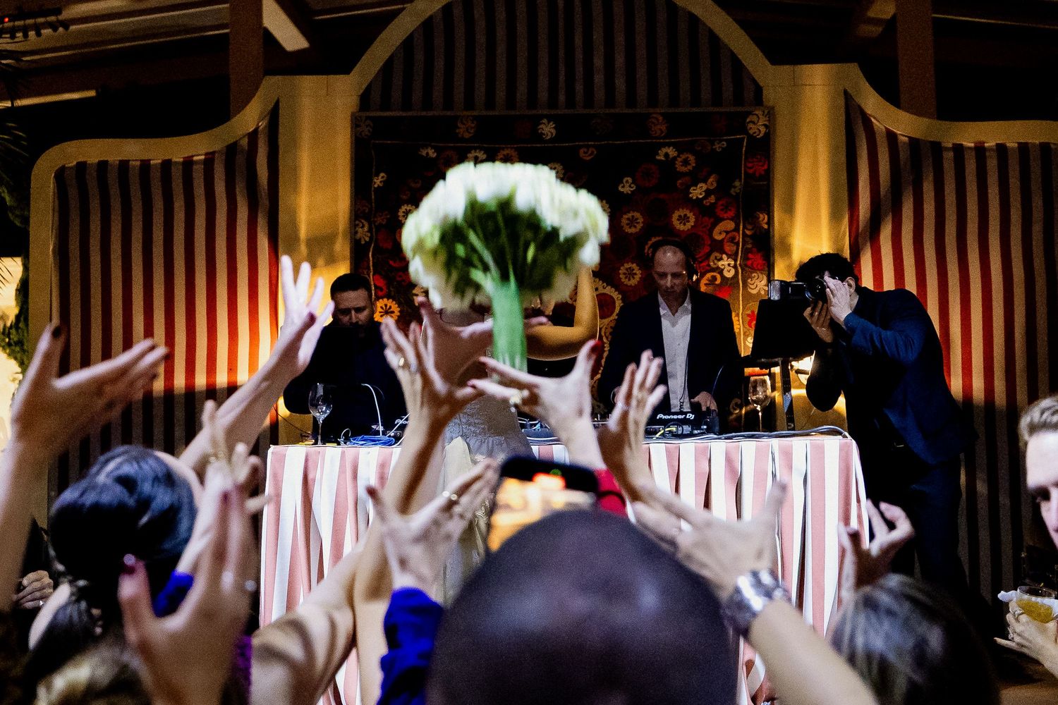 Wedding guests dance and celebrate on a festively decorated dance floor at an indoor reception venue.