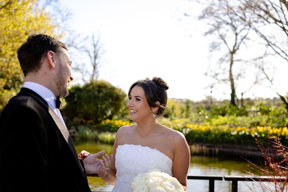 Bride and groom embrace in a romantic outdoor setting with a lake and fall foliage in the background.