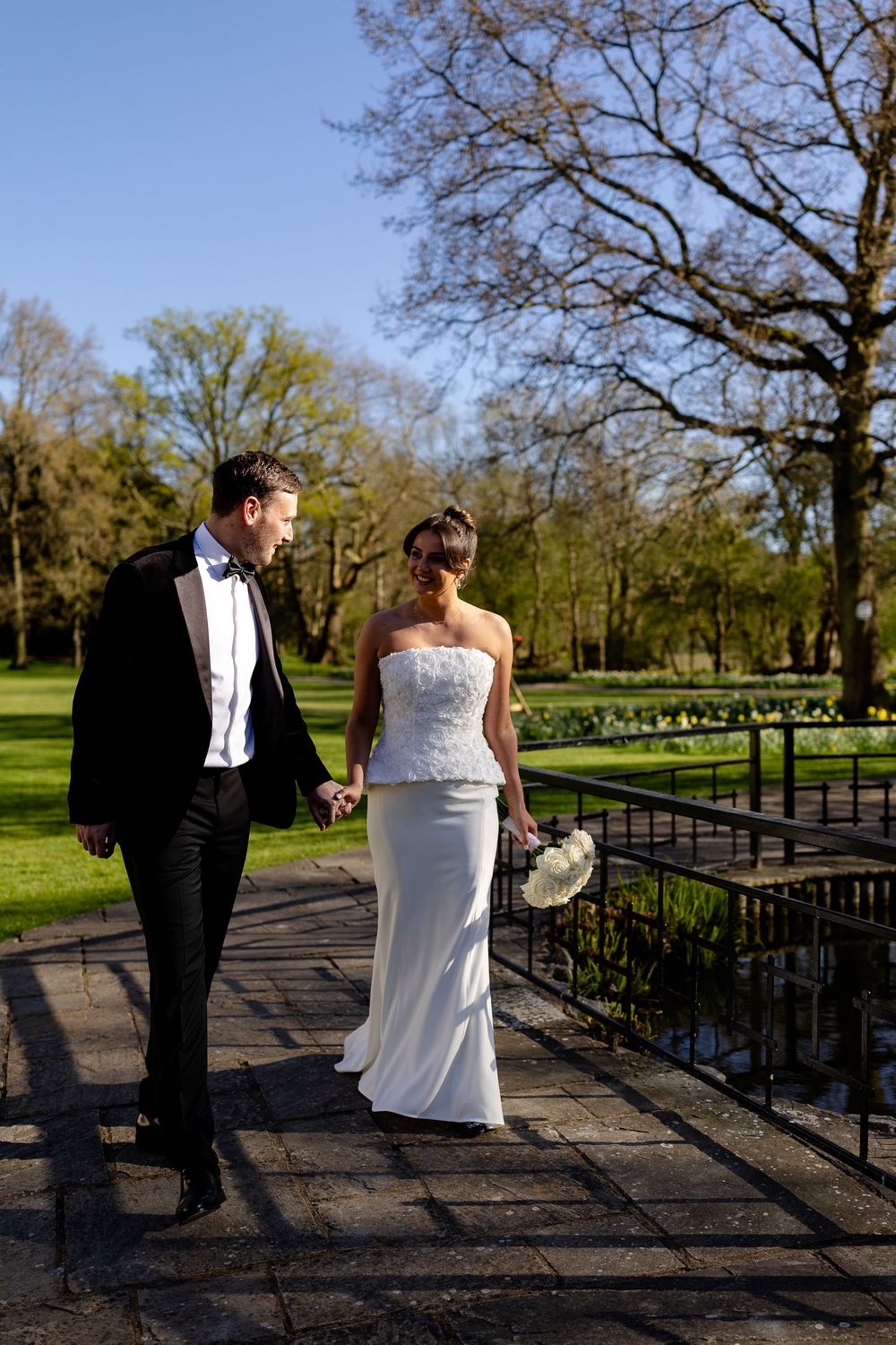 Wedding couple walking along a scenic pathway surrounded by spring trees and greenery.