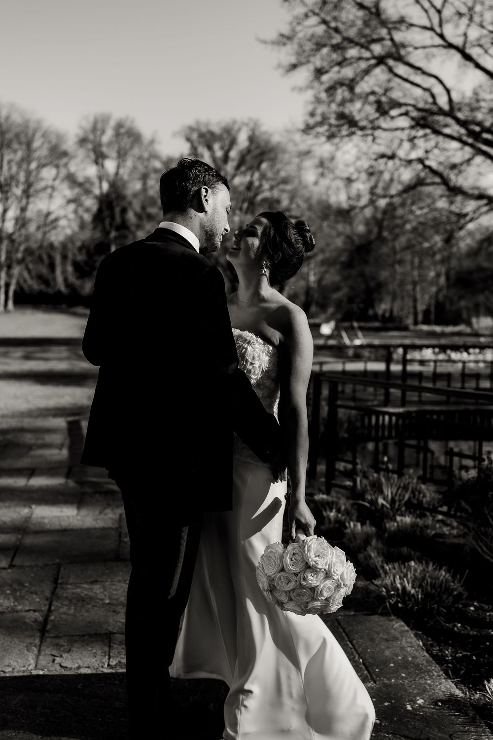 Black and white wedding portrait of a couple in a rustic outdoor setting with trees.