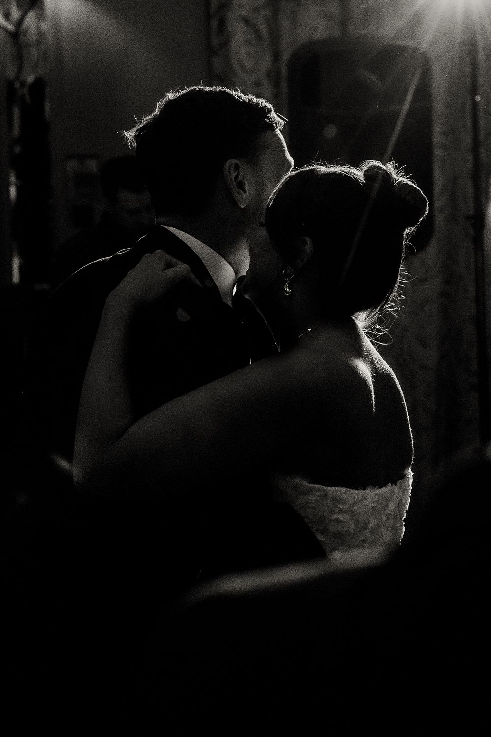 Romantic silhouettes of couples dancing together at a dimly lit wedding reception.