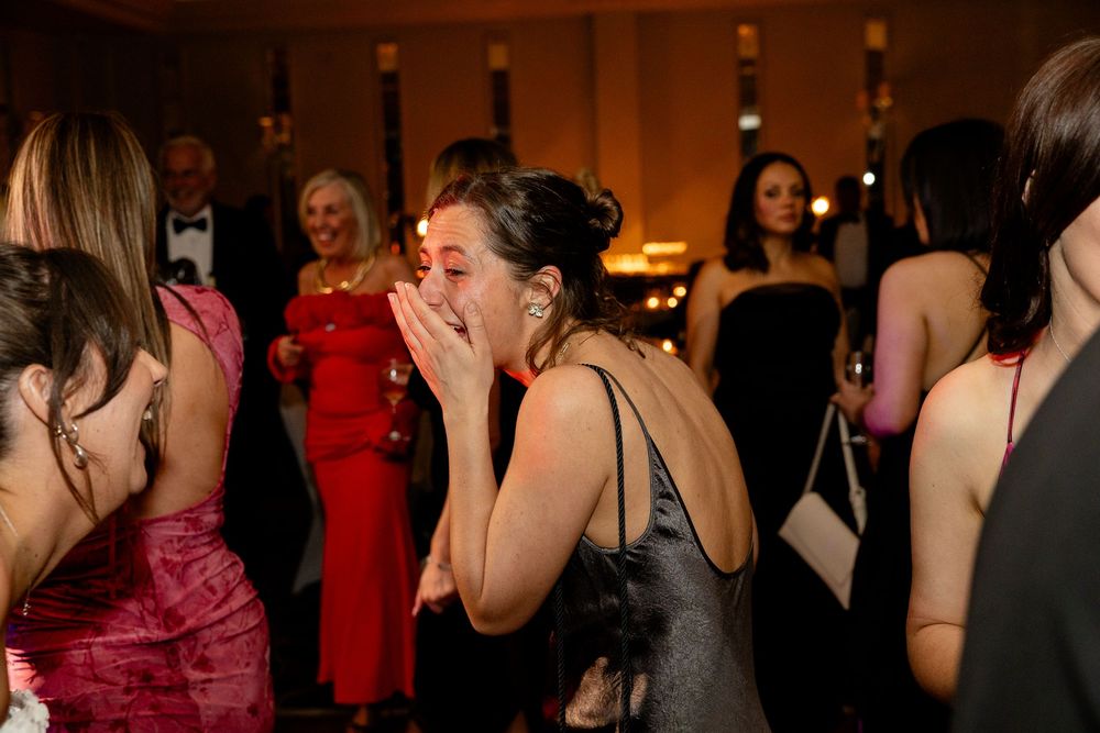 Wedding reception guests dancing and celebrating in a warmly lit ballroom with red accents.