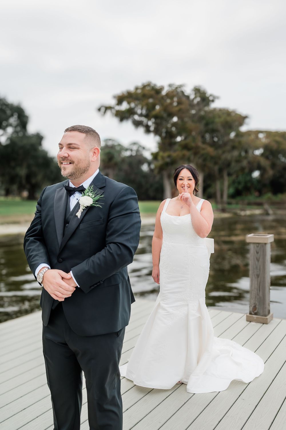 A couple shares an emotional first look moment on a wooden dock by a lake during their wedding day.