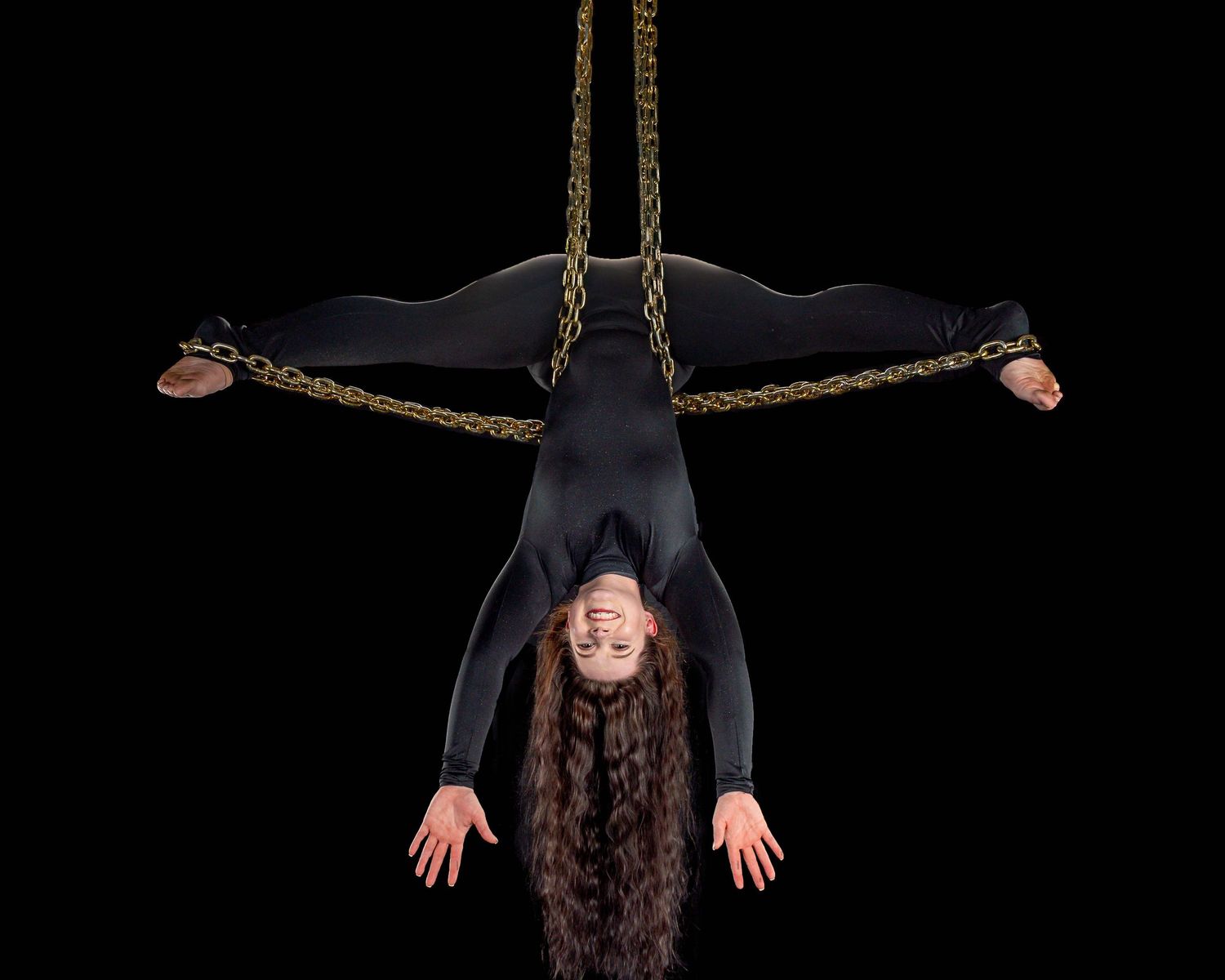 A person hangs upside down from ropes in a dark studio setting, creating a dramatic silhouette against the black background.