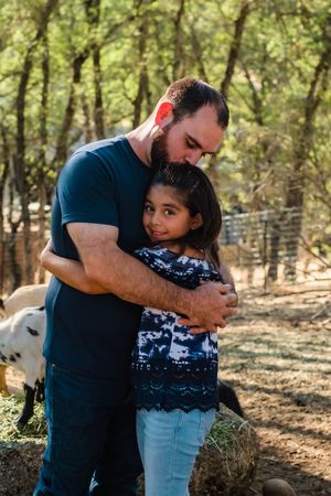 Carlos hugs his daughter in a sunlit wooded area of their back yard in valley springs california