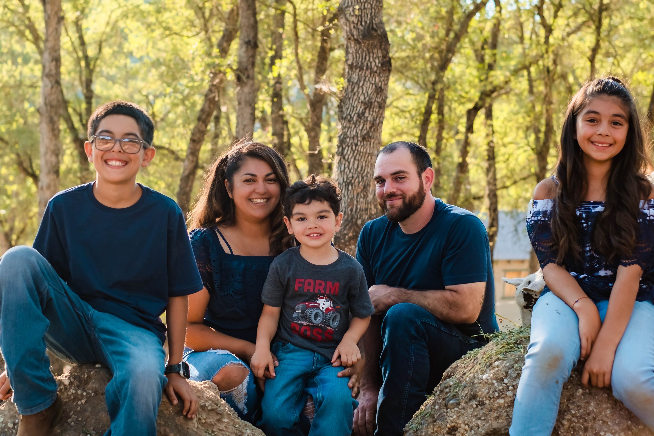 Sue & Carlos sitting on the rocks and hay in their backyard with the animals in valley springs ca