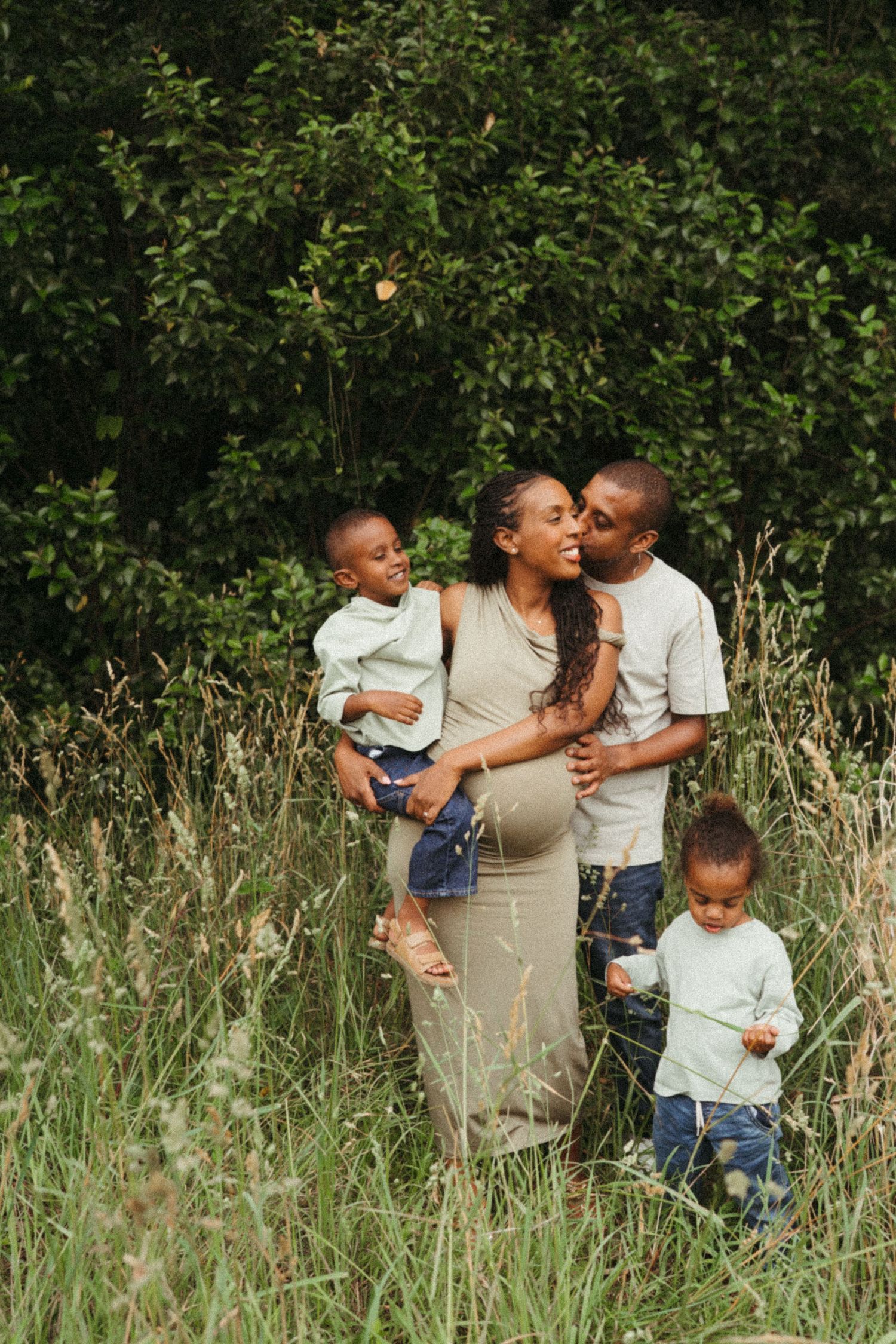 Family sharing tender moments together in tall grass and greenery.