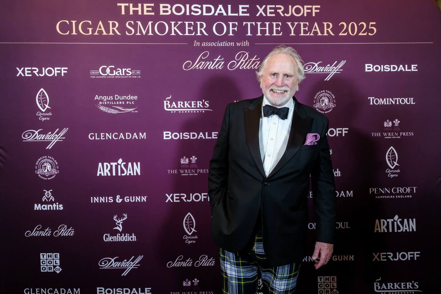 Guests pose against a purple step-and-repeat banner wall featuring luxury brand logos at an upscale event.