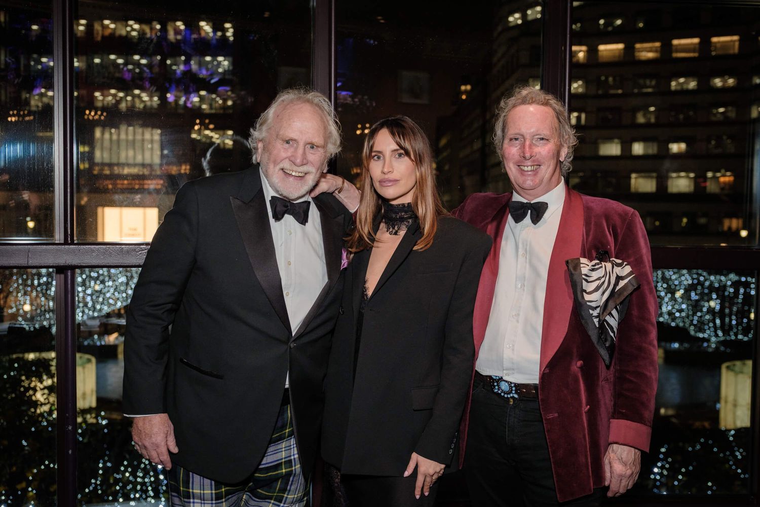 Guests in formal attire including tuxedos and evening gowns gather at an elegant nighttime event.