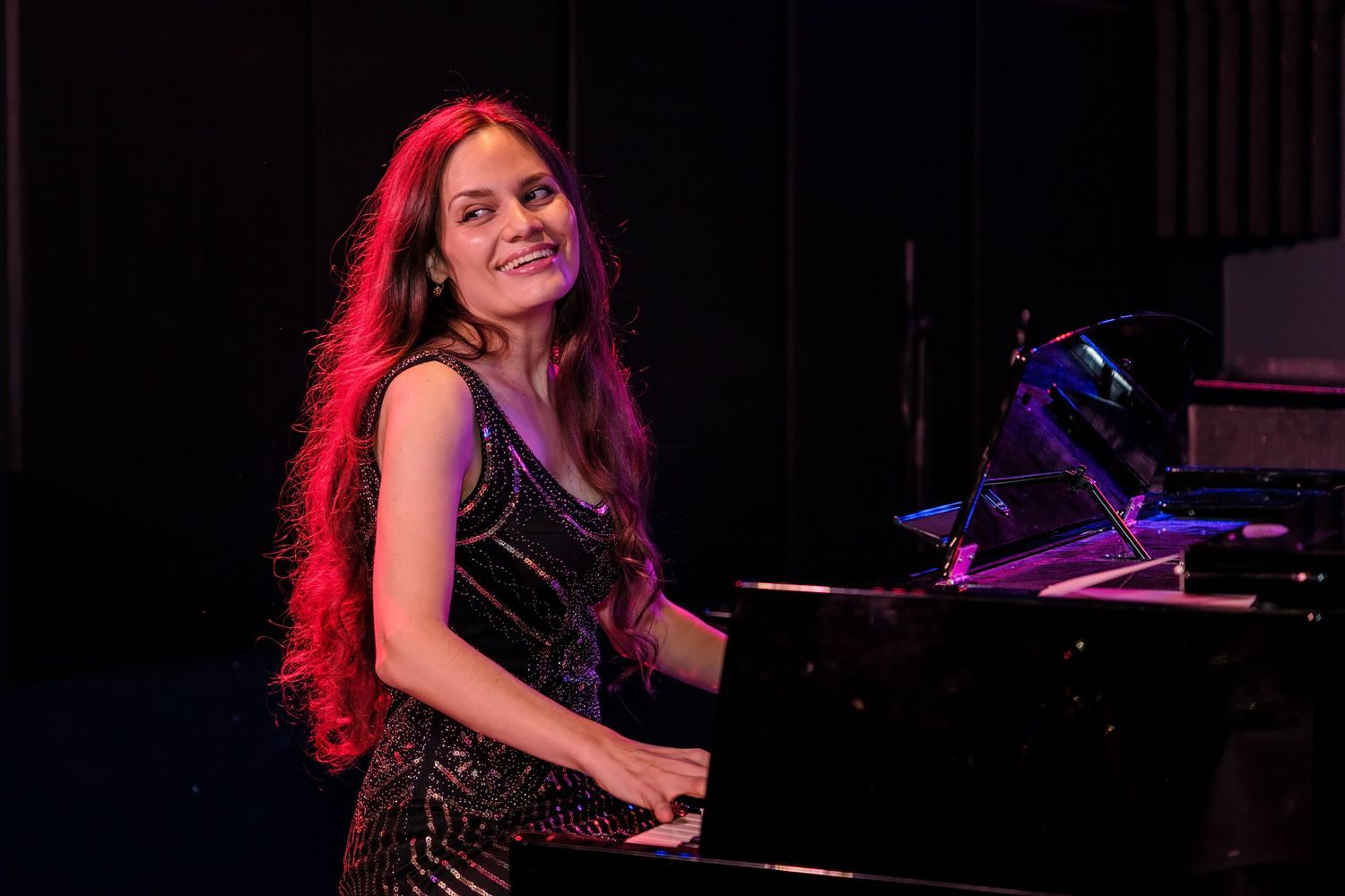 A performer plays piano on stage illuminated by dramatic red lighting during a live performance.
