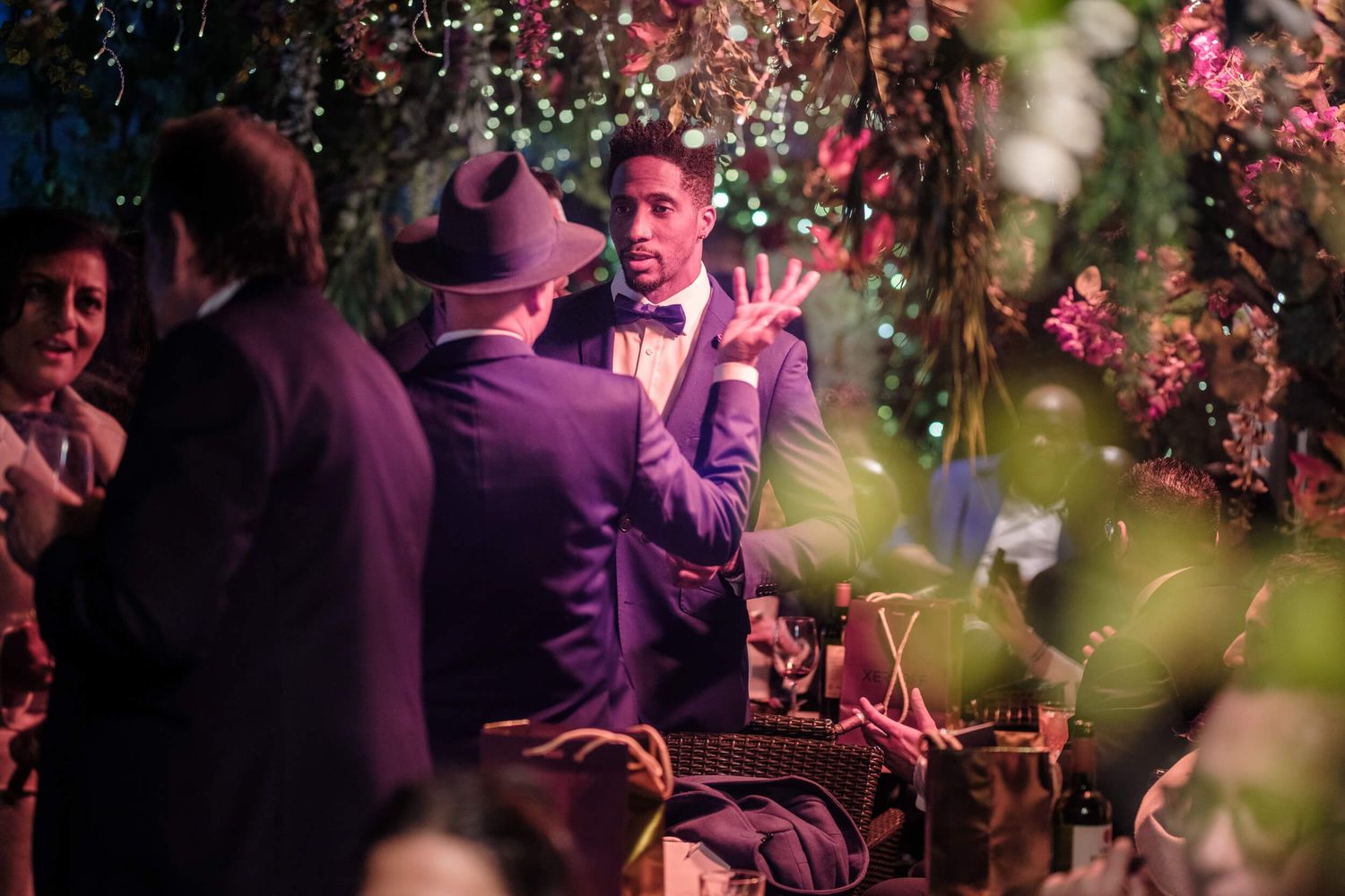 Colorful cherry blossoms frame a nighttime party scene with people dancing and celebrating in purple lighting.