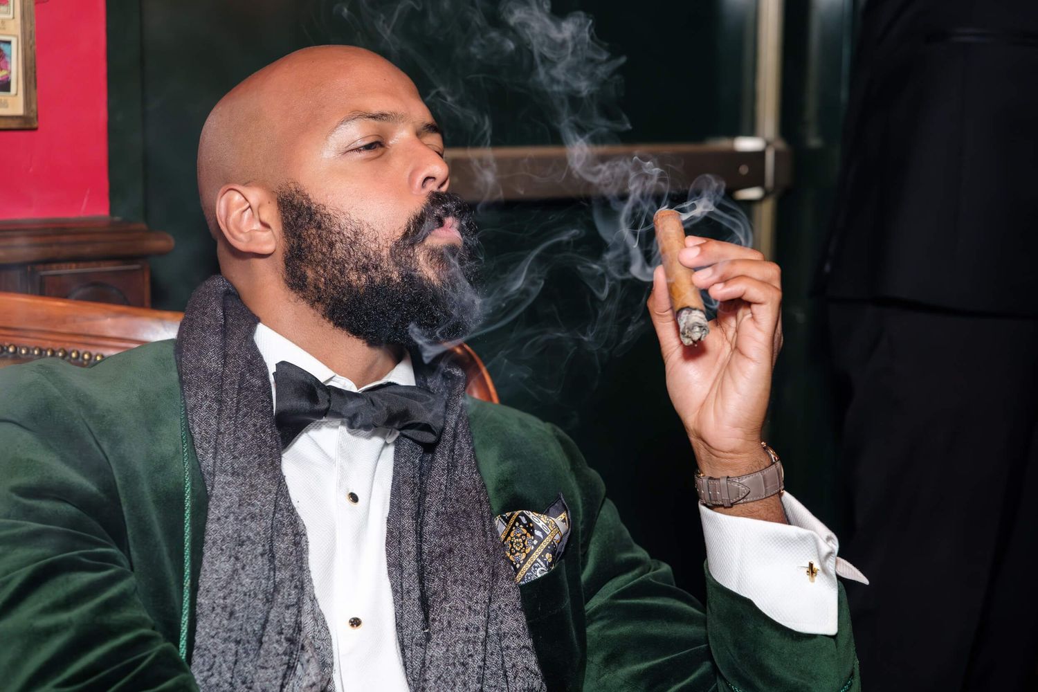 A person in a tuxedo exhales cigar smoke while enjoying a luxurious evening.