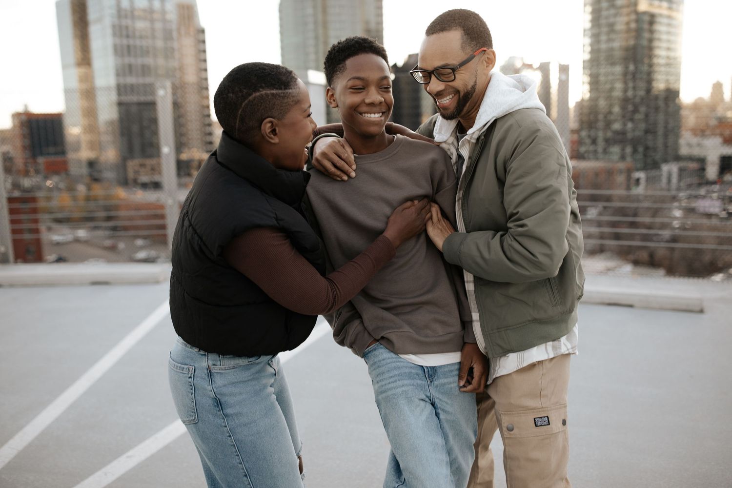Friends sharing laughs and embracing on a rooftop parking area with urban backdrop.