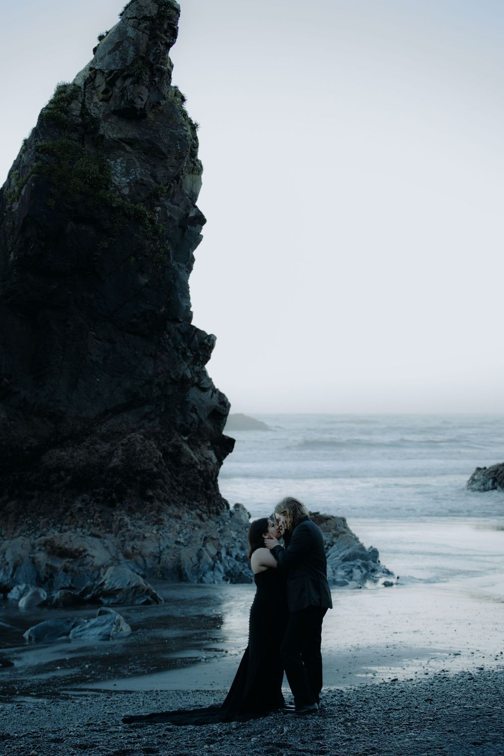 Romantic coastal photography featuring two people against dramatic seaside cliffs.