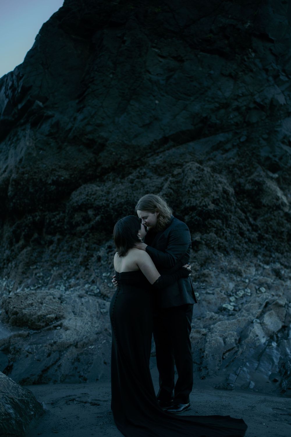 Silhouettes of a couple embracing against dark coastal cliffs at dusk.