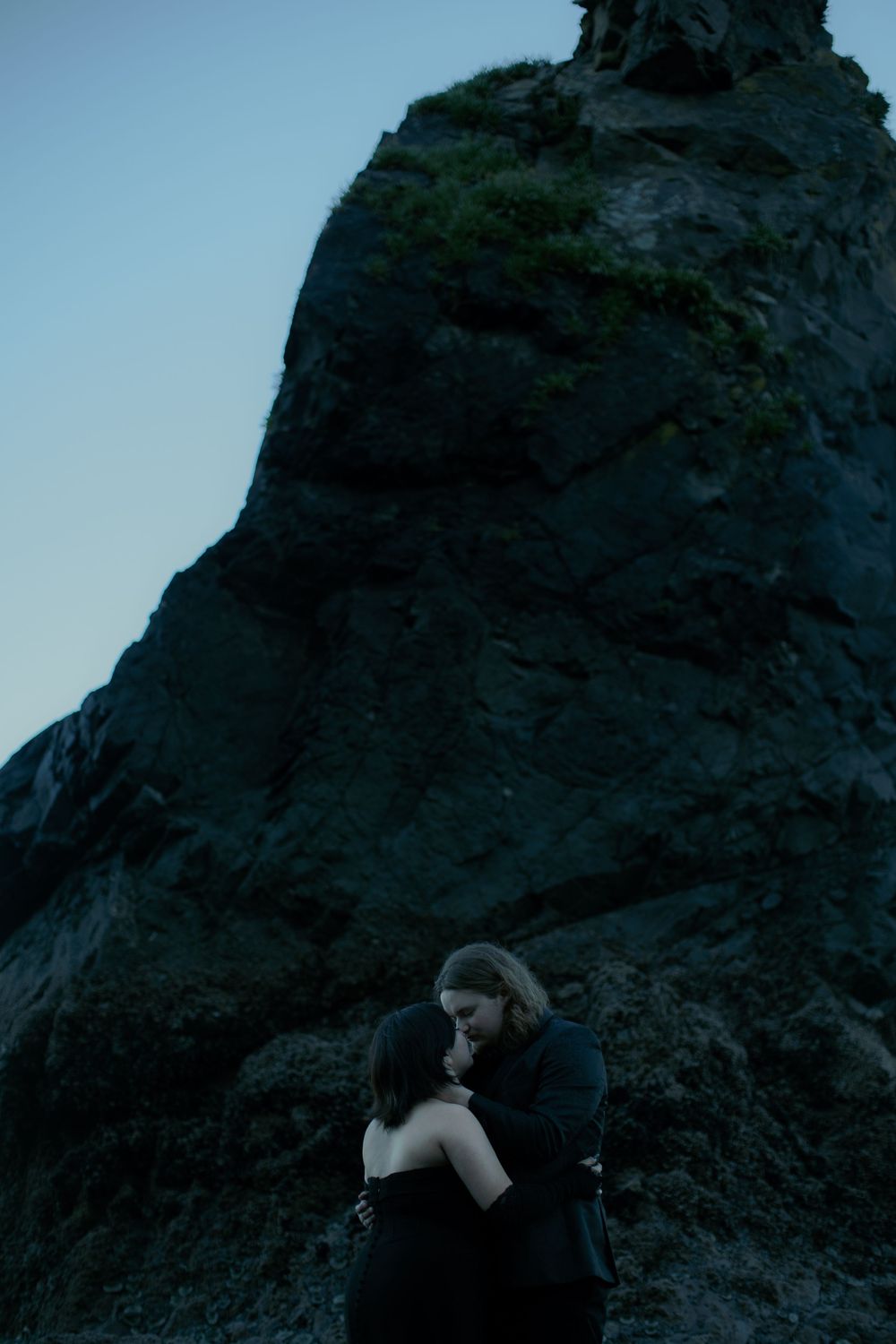 Dramatic seaside scene with dark rocky cliffs and intimate moment.