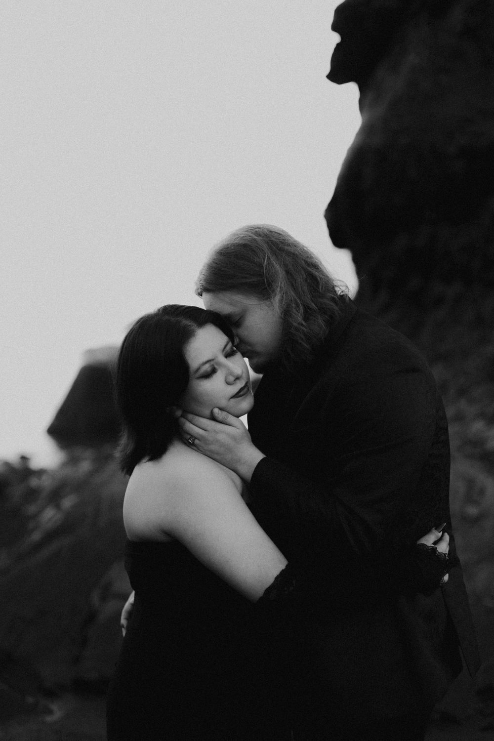 Black and white romantic portraits showing tender embraces against dark rocks.