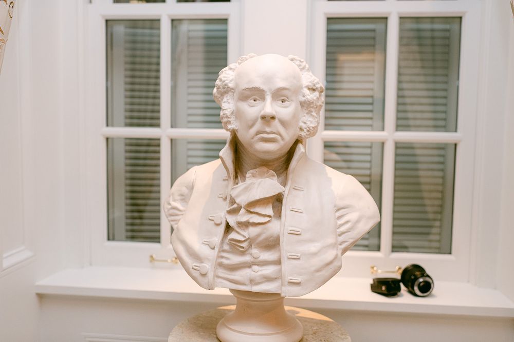 A row of marble busts and sculptures displayed in front of windows at a museum or gallery.