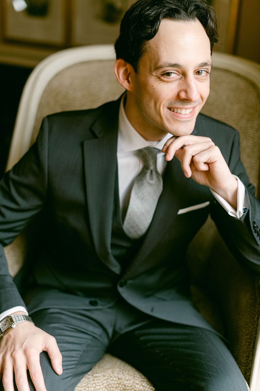 Professional wearing a dark suit and tie sits casually while smiling in an indoor setting.