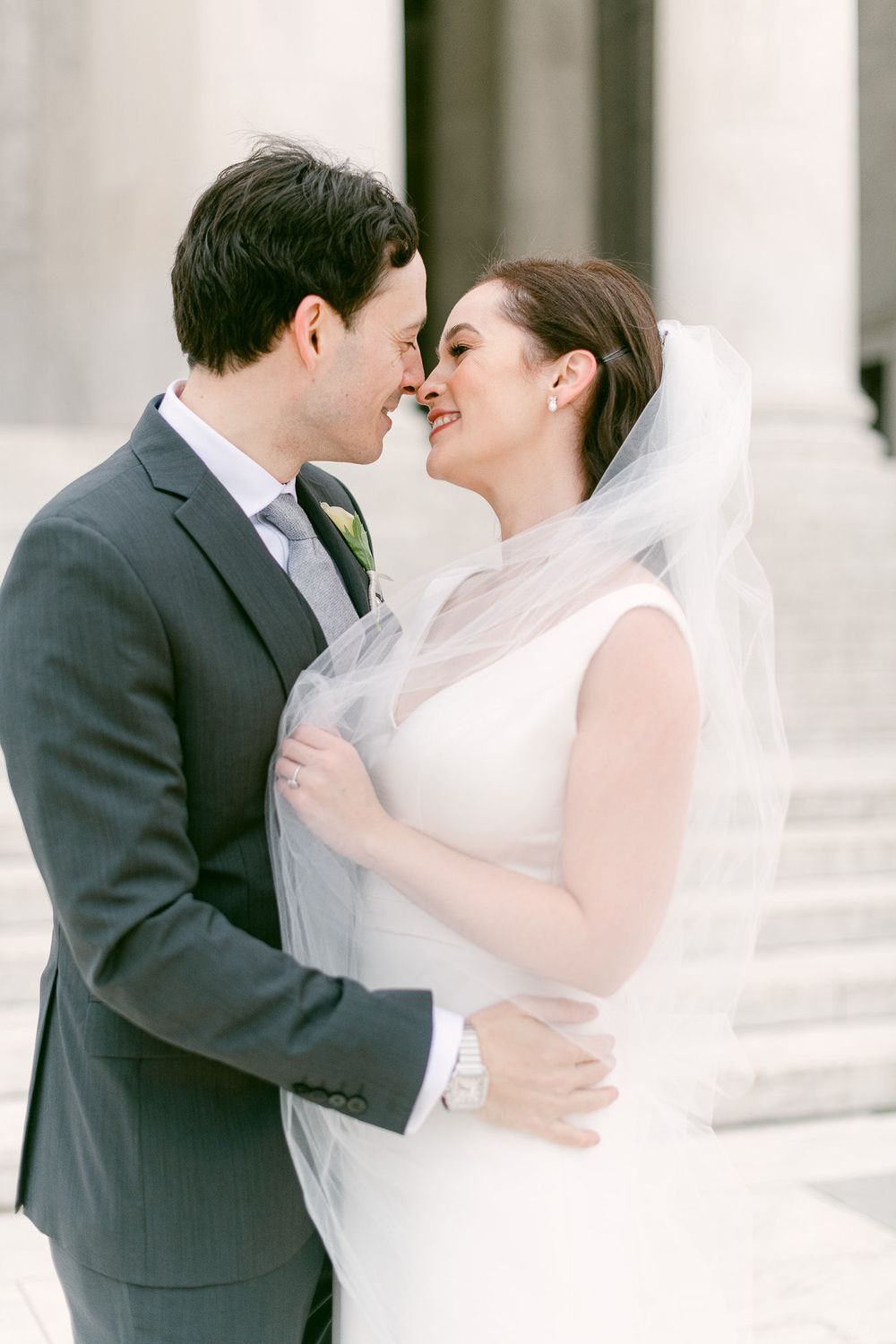 Romantic wedding couple sharing an intimate kiss with a flowing white veil in an elegant setting.