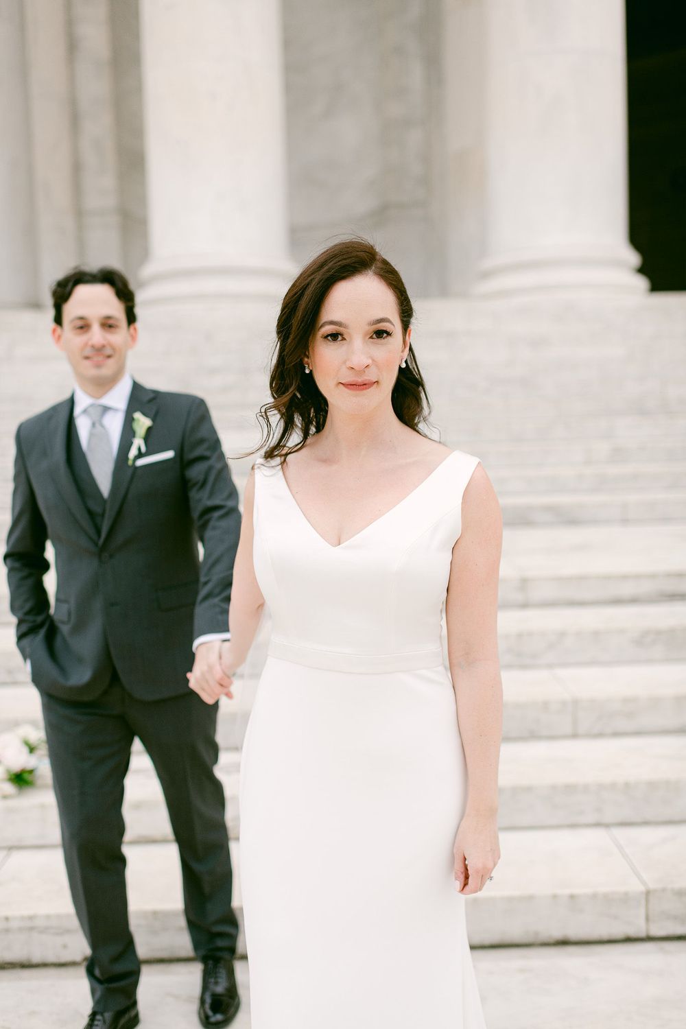 Wedding party members walk elegantly across white stone steps of a classical building.