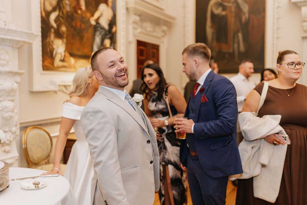 Wedding guests enjoying drinks and conversation during an elegant indoor reception at a historic venue.