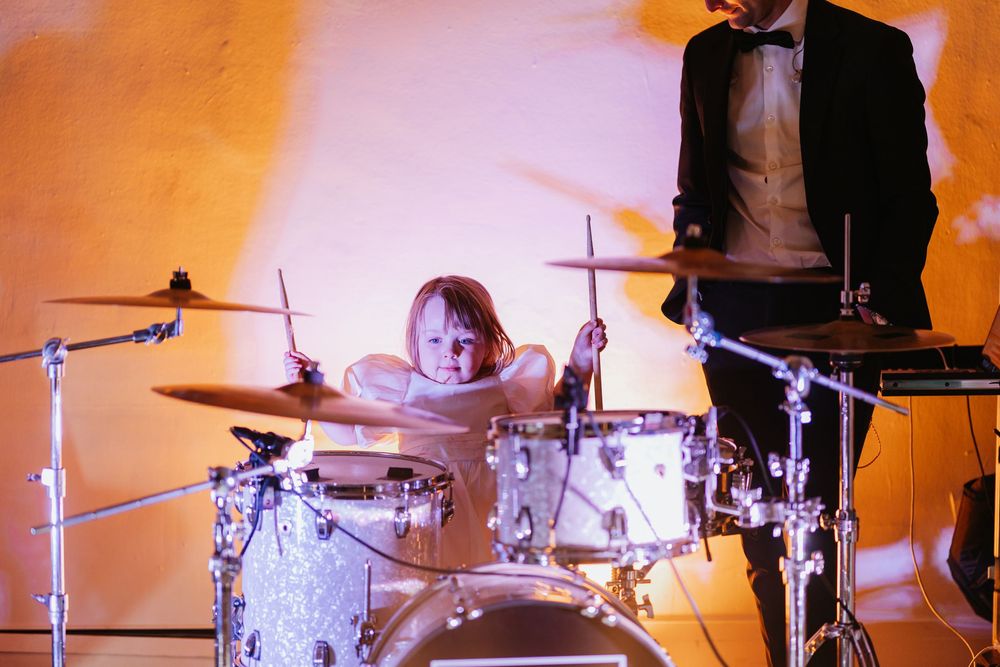 Drummer performs energetically on stage with orange lighting and drum kit setup during a live music performance.
