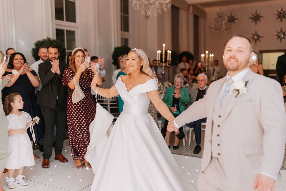 Wedding guests dance and celebrate together at an elegant indoor reception venue with white decor.