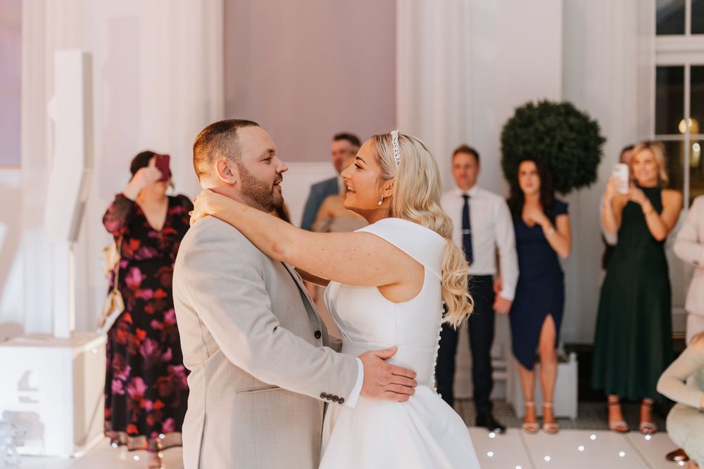 Wedding reception dance floor filled with guests celebrating and dancing in an elegant white-walled venue.