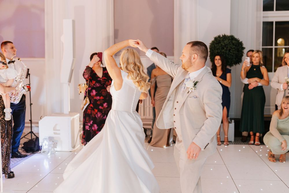 A dancing couple performs a twirl during their wedding celebration as guests look on in a bright venue.