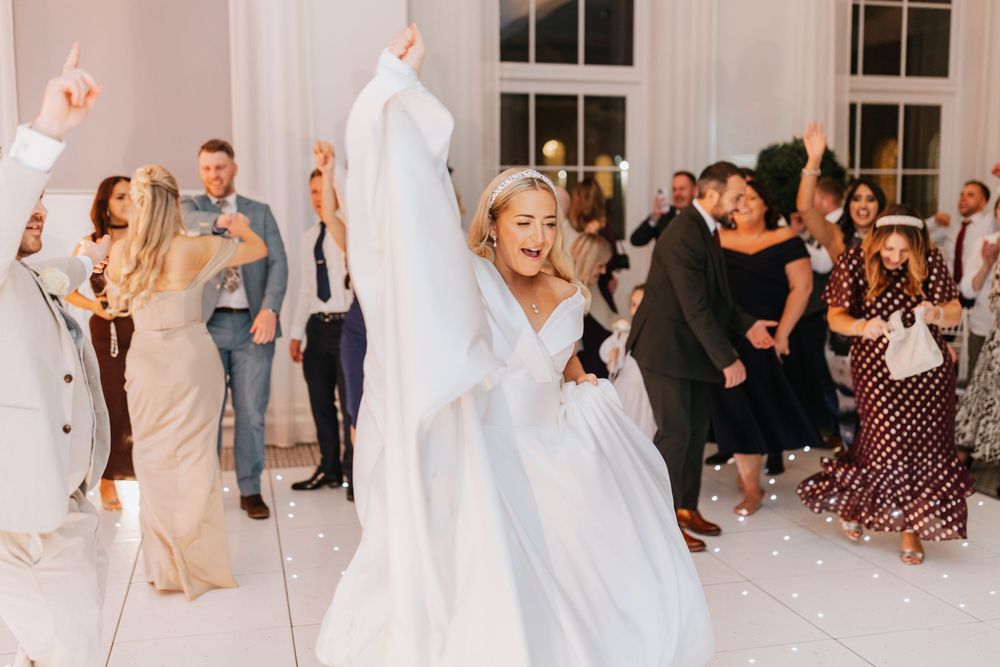Wedding guests dancing and celebrating together on a white dance floor at an elegant reception venue.