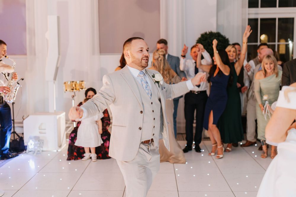 Wedding guests dance and celebrate on a brightly lit dance floor during an evening reception.