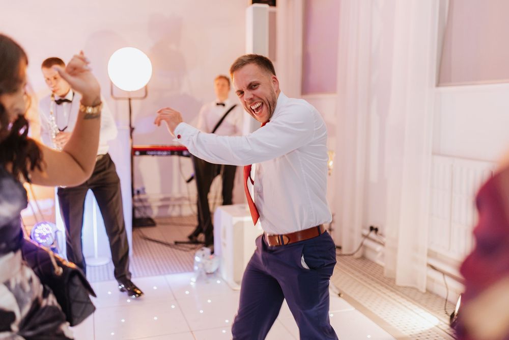 People dancing and having fun at a wedding reception in a bright white venue with party lighting.