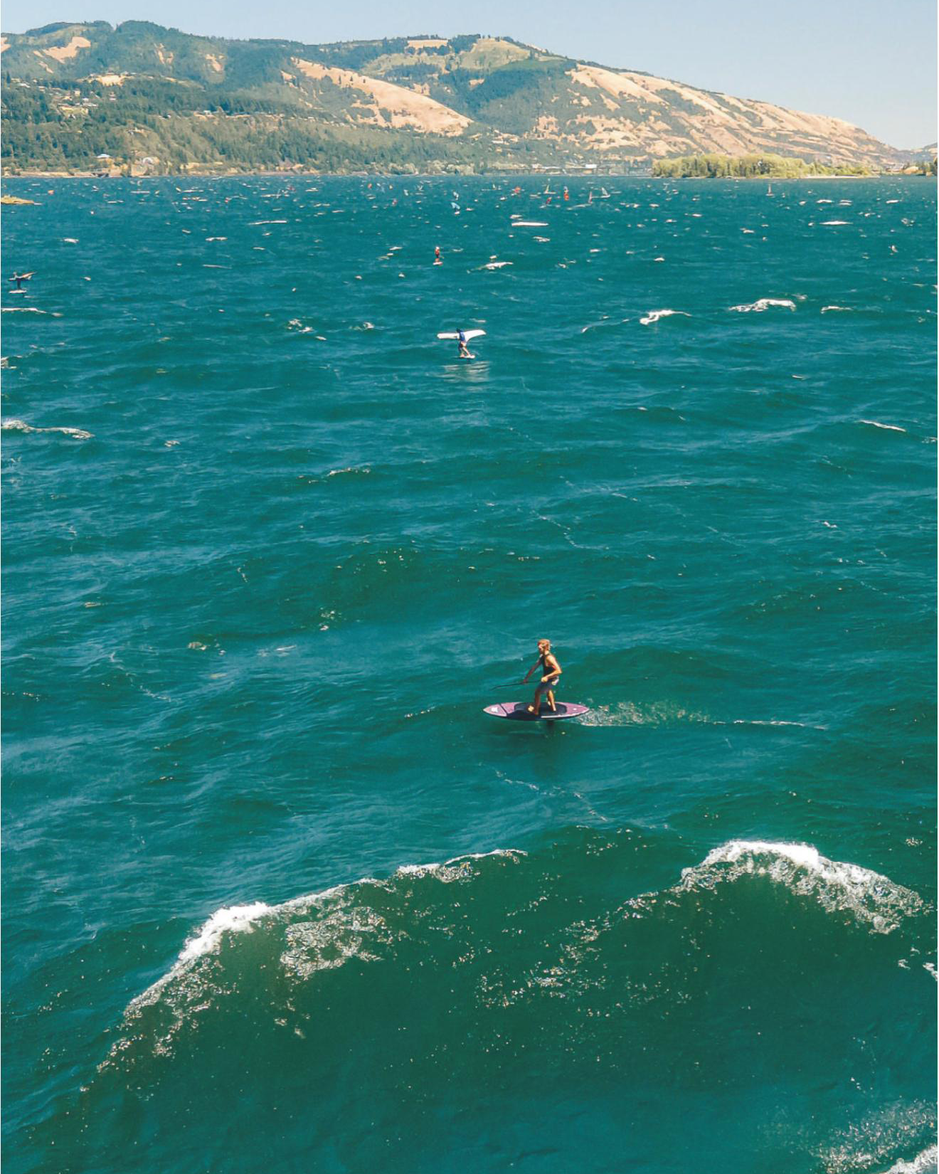 Turquoise ocean waves ripple beneath distant mountain ranges on a sunny day.