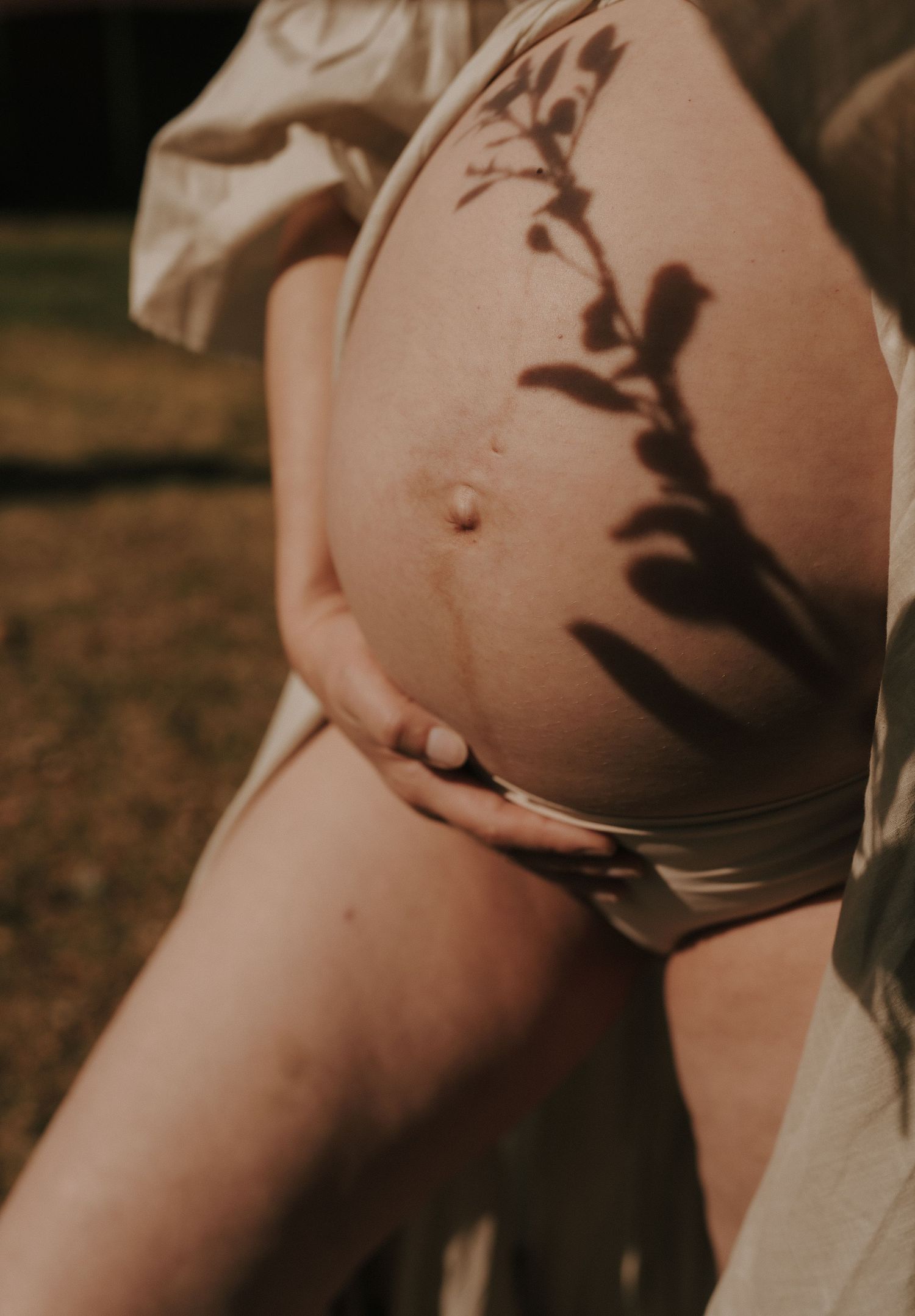 Warm-toned artistic maternity photo with leaf shadows.