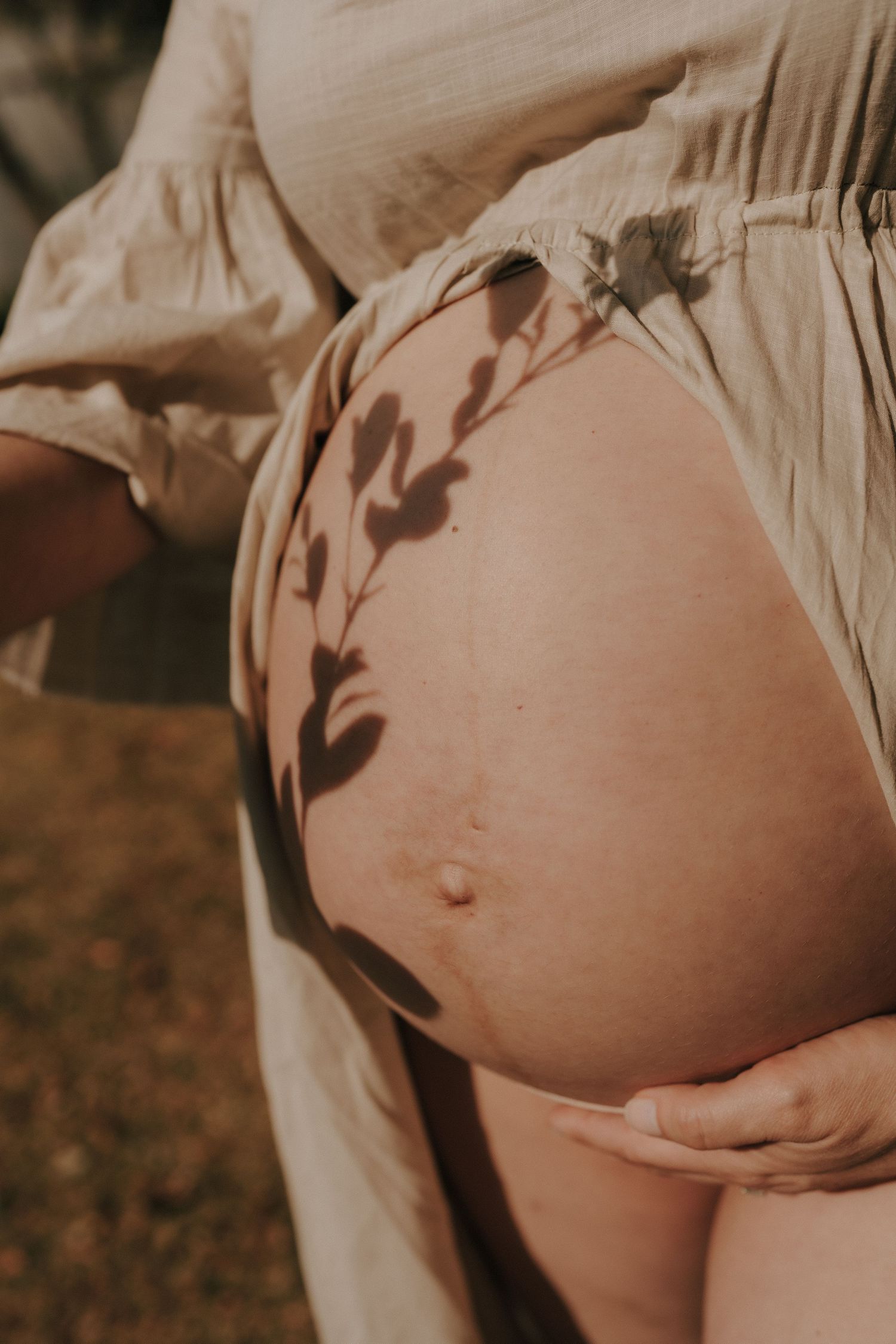 Artistic maternity portrait with natural light and leaf shadows.