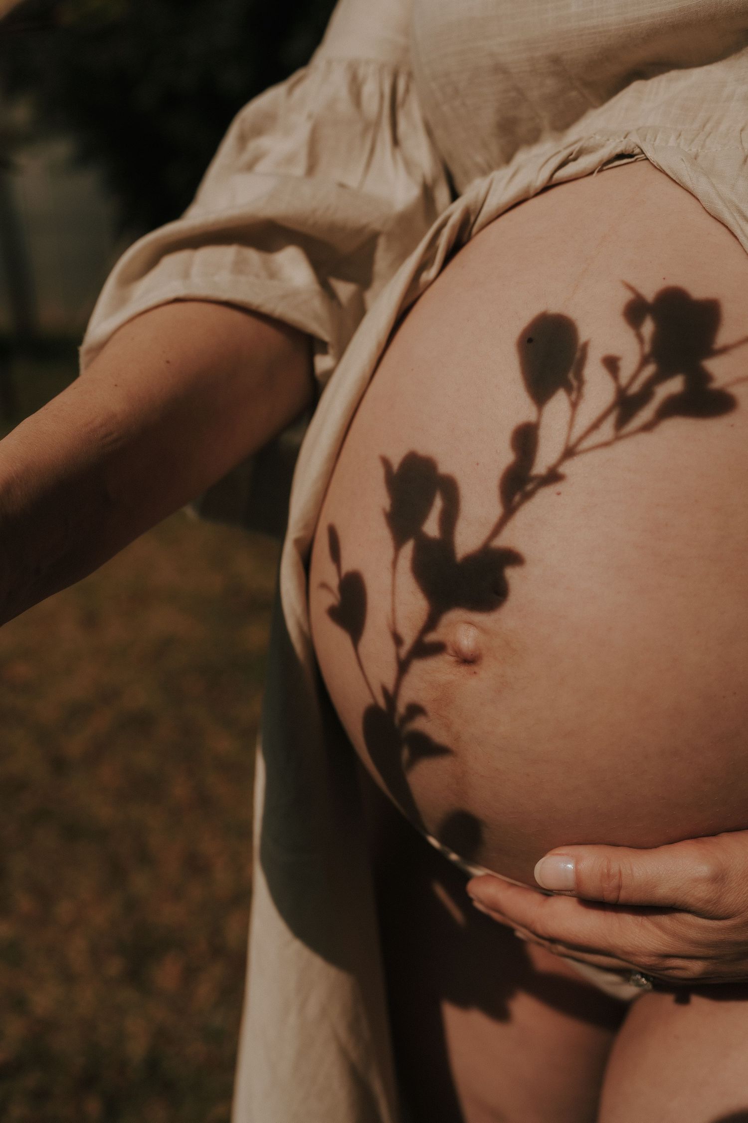 Close-up maternity photo showing delicate leaf shadows on pregnant belly.