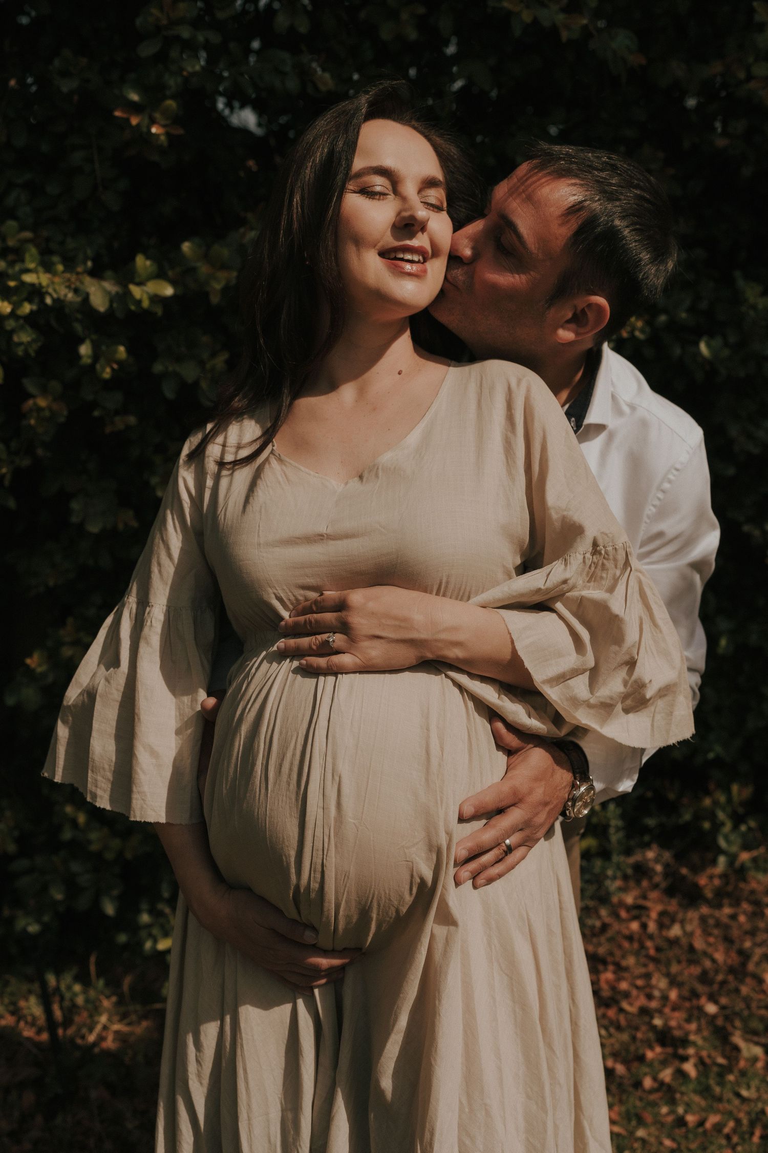 Intimate maternity portraits captured in natural lighting with a couple in cream-colored clothing against autumn foliage.