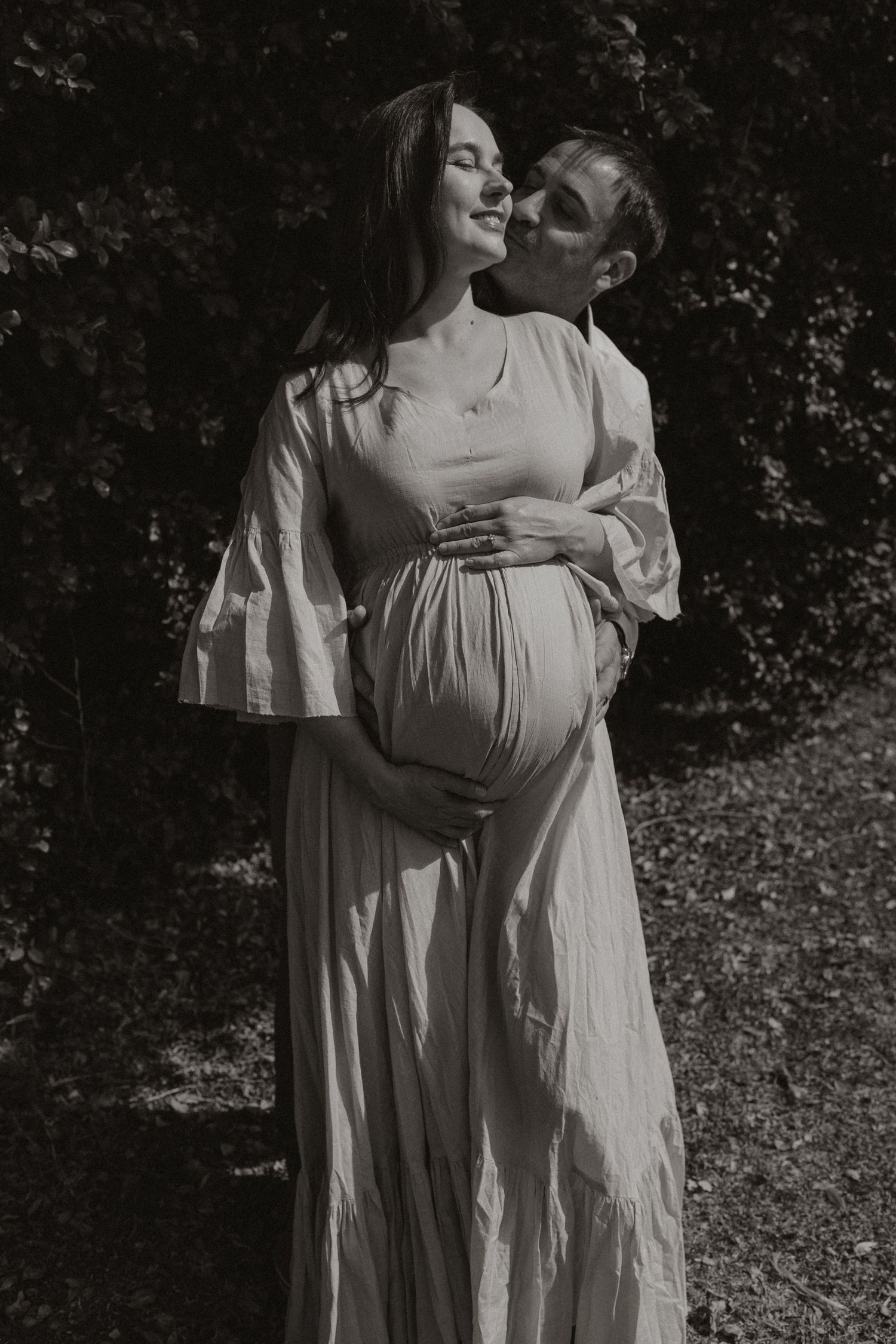 Dreamy black and white maternity photos featuring gentle embraces and flowing white dresses in a natural setting.