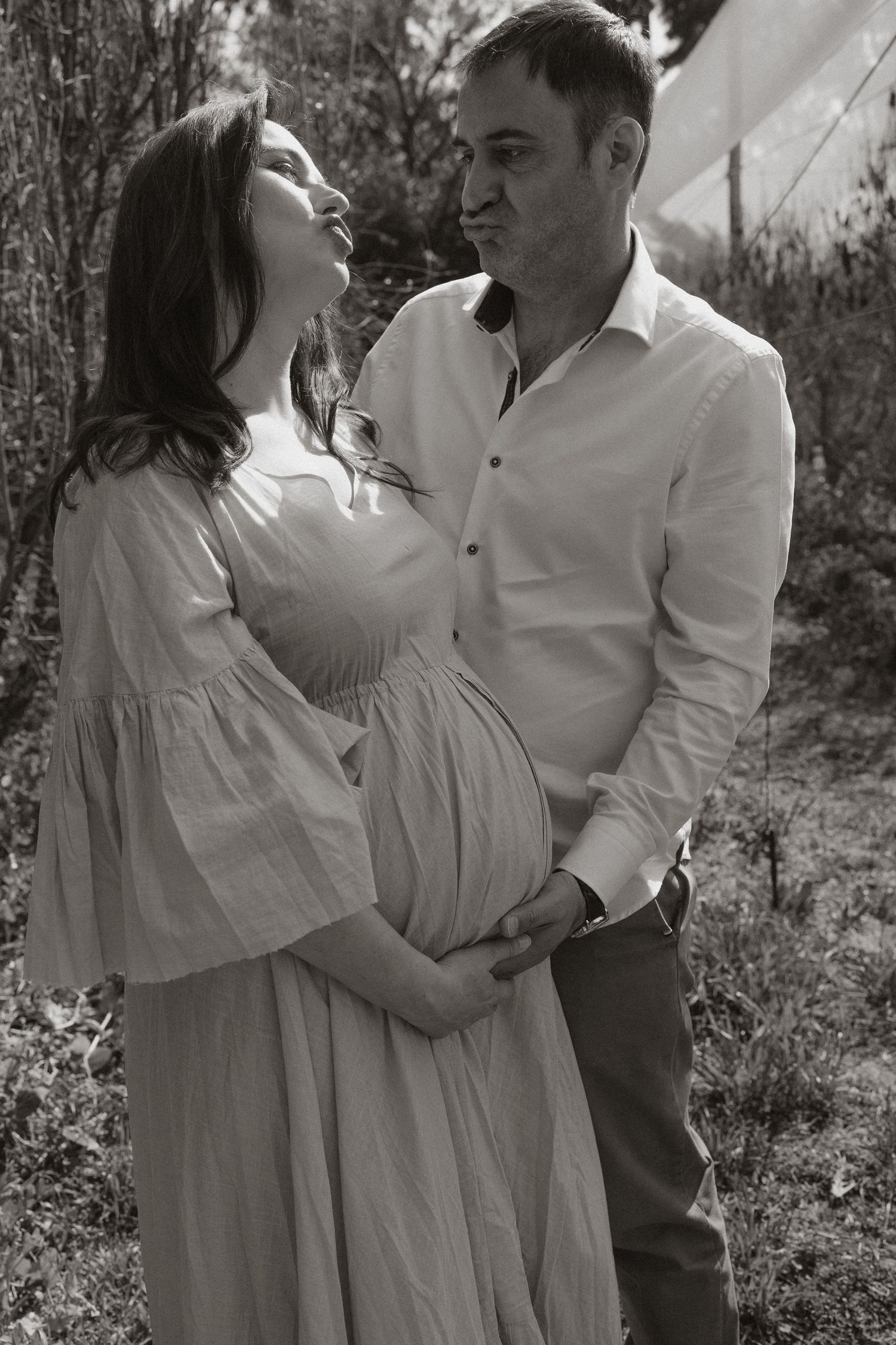 Black and white portrait of a couple sharing affectionate moments in a natural outdoor setting.