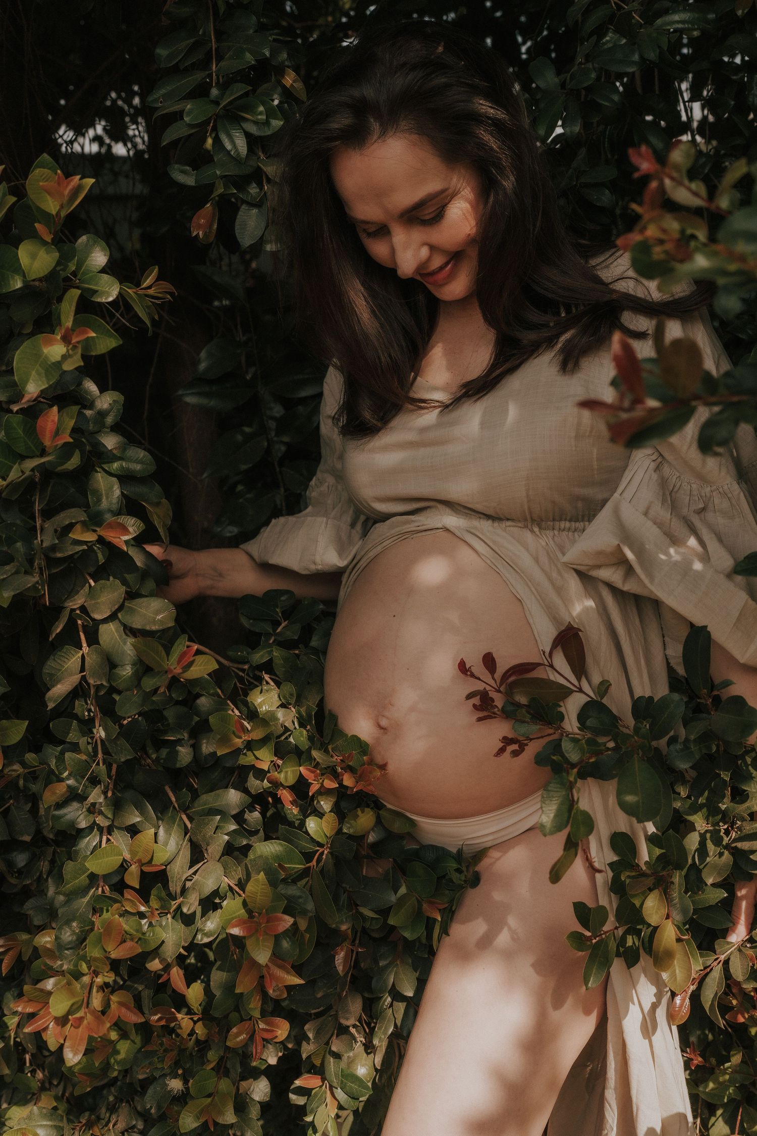Artistic maternity photo featuring a flowing white dress amidst lush greenery and natural lighting.
