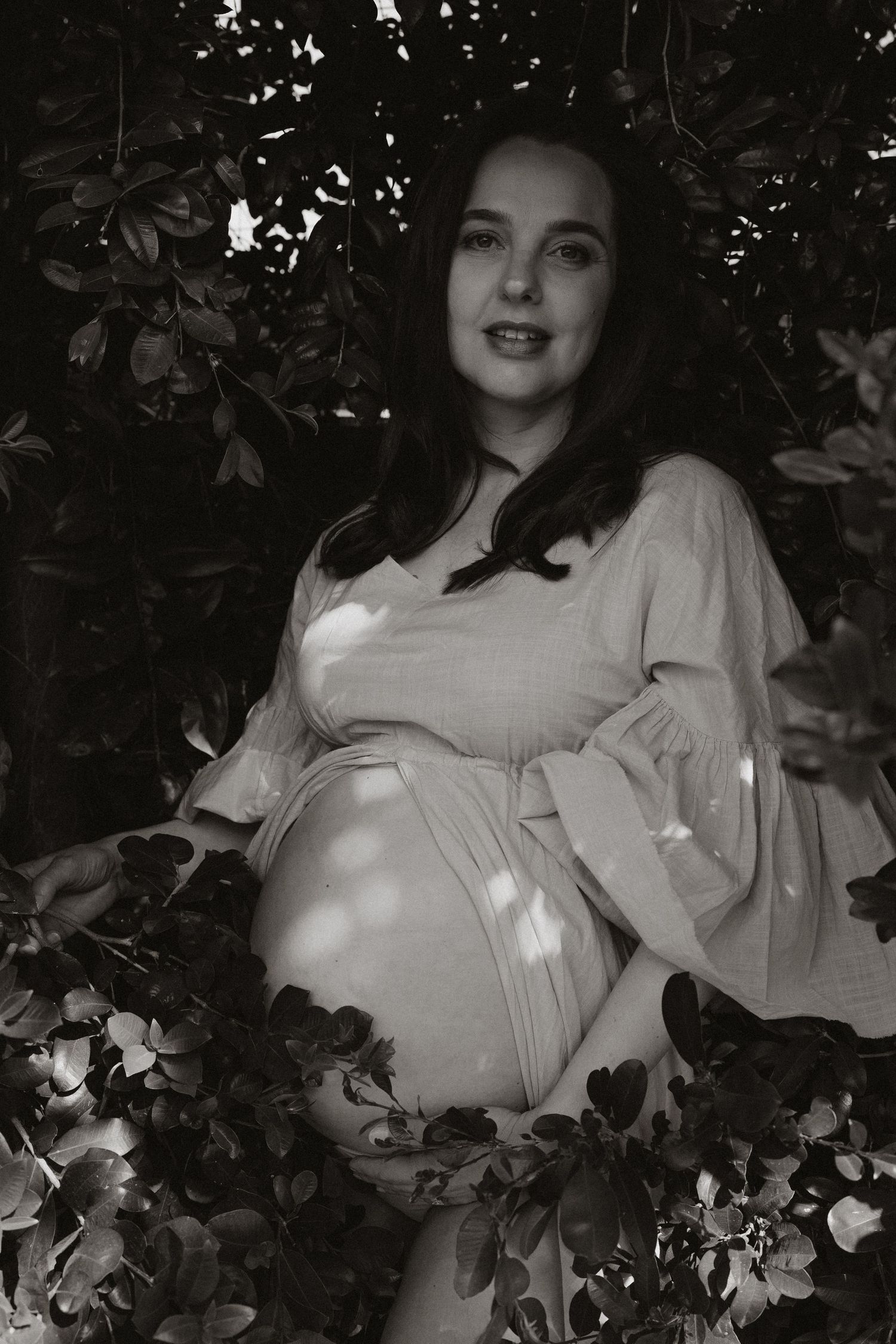 Dramatic maternity photo with vintage styling amidst garden greenery.