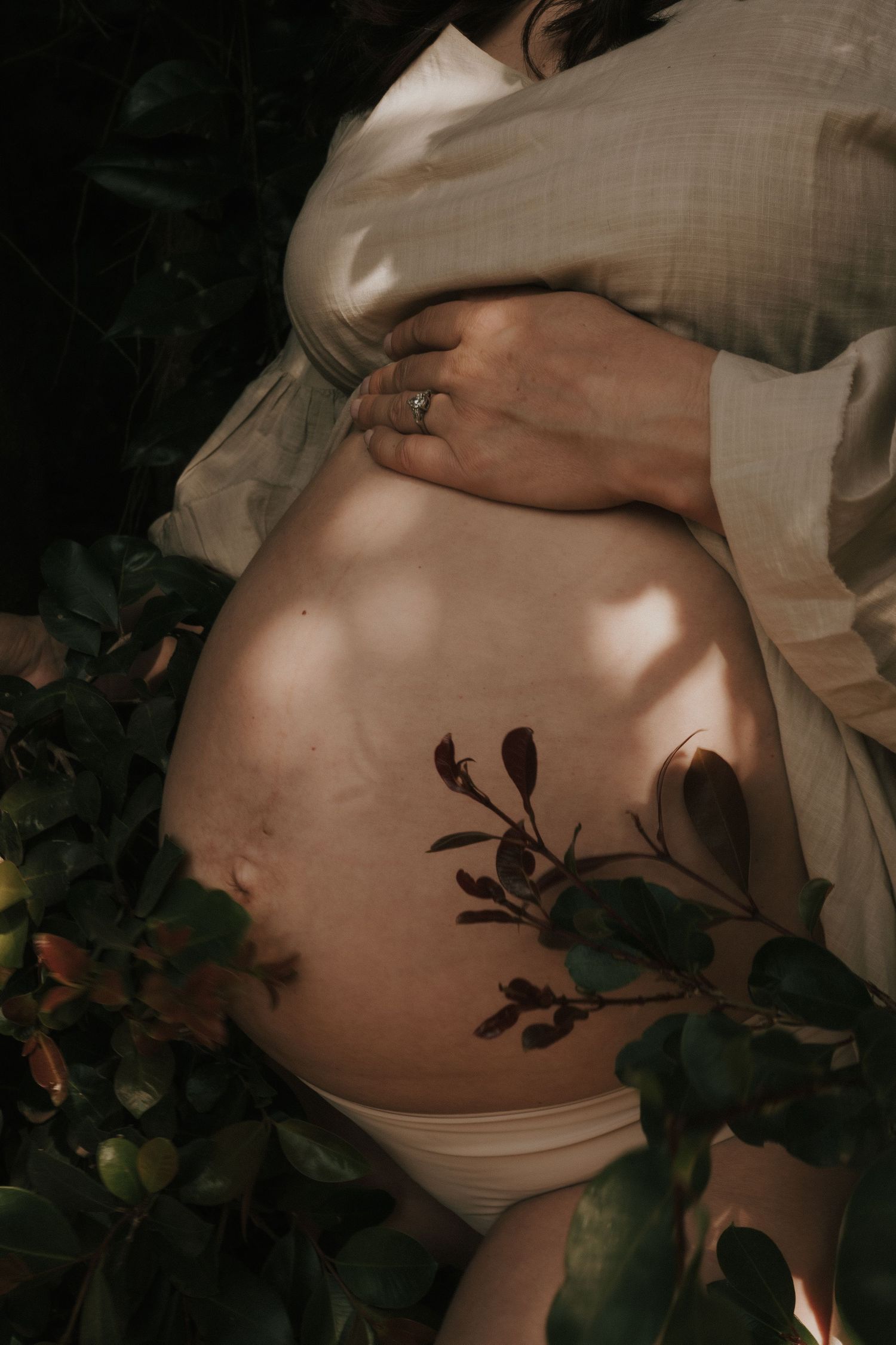 Close-up of pregnant belly with leaf shadows creating artistic patterns.