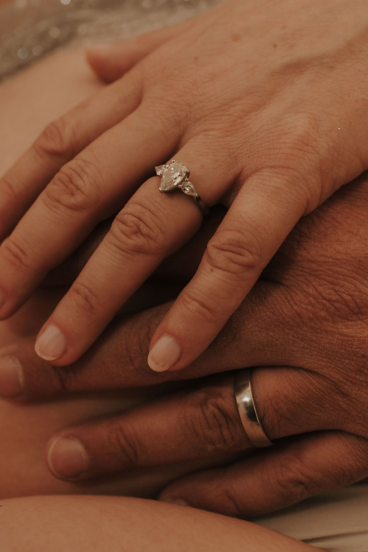 Close-up of intertwined hands showing wedding rings against warm-toned background.